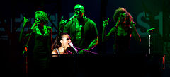 Keys playing the piano while performing, surrounded by three backing vocalists