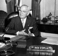 Truman poses in 1959 at the recreation of the Truman Oval Office at the Truman Library in 1959, with the famous "The Buck Stops Here" sign on his desk.