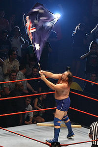 Duggan waving an Australian flag during his ring entrance in Australia, 2007, with his 2x4 in the corner