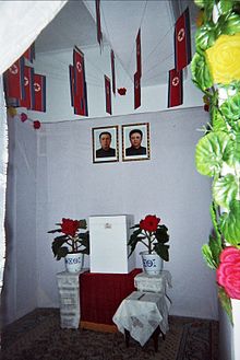A North Korean voting booth containing portraits of Kim Il-sung and Kim Jong-il under the national flag. Below the portraits is the ballot box.