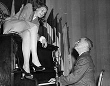 Bacall sits atop the piano while Vice President Harry S Truman plays the piano at the National Press Club Canteen. (February 10, 1945)