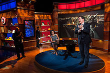 Colbert, in his television series persona, prepares to interview Michelle Obama. The set of The Colbert Report satirizes cable-personality political talk shows.