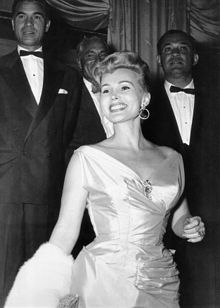 At a social affair, c. 1954 accompanied by international playboy and diplomat Porfirio Rubirosa (behind her, to the left)