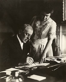 Woodrow Wilson's first posed photograph after his stroke. He was paralyzed on his left side, so his wife Edith holds a document steady while he signs. June 1920.